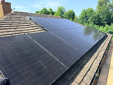 Rooftop solar array fitted to mossy clay tiles with a mesh critter guard and a brick chimney stack
