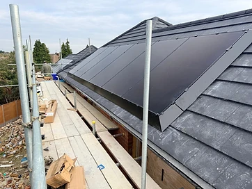 Row of black solar panels integrated into a slate-tiled roof beside a scaffolding platform during installation
