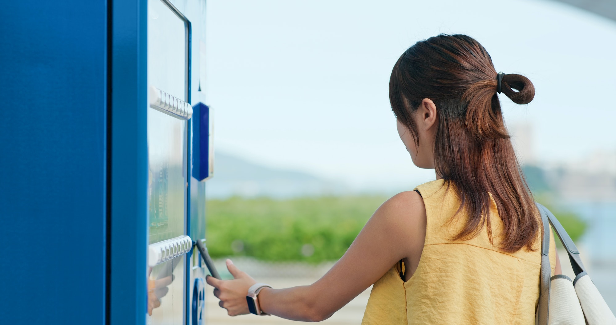 Woman using mobile phone to buy a drink at a vending machine