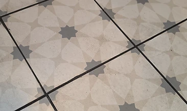 Scuffed, grimed tile floor in a high-traffic commercial kitchen. Grout lines blackened with embedded grease and soil requiring deep extraction.