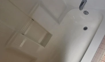 Tub and shower enclosure with chrome valve controls. Soap scum, hard water rings, and discoloration on surround walls and basin.