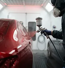 Process step: technician applying factory-grade color-matched paint in a clean, professional refinishing booth