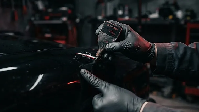 Technician performing a quality-control inspection on a refinished vehicle panel