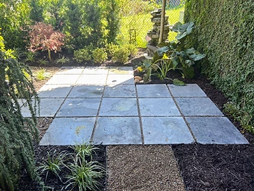Square grey slate patio framed by mulch beds and a stone fountain