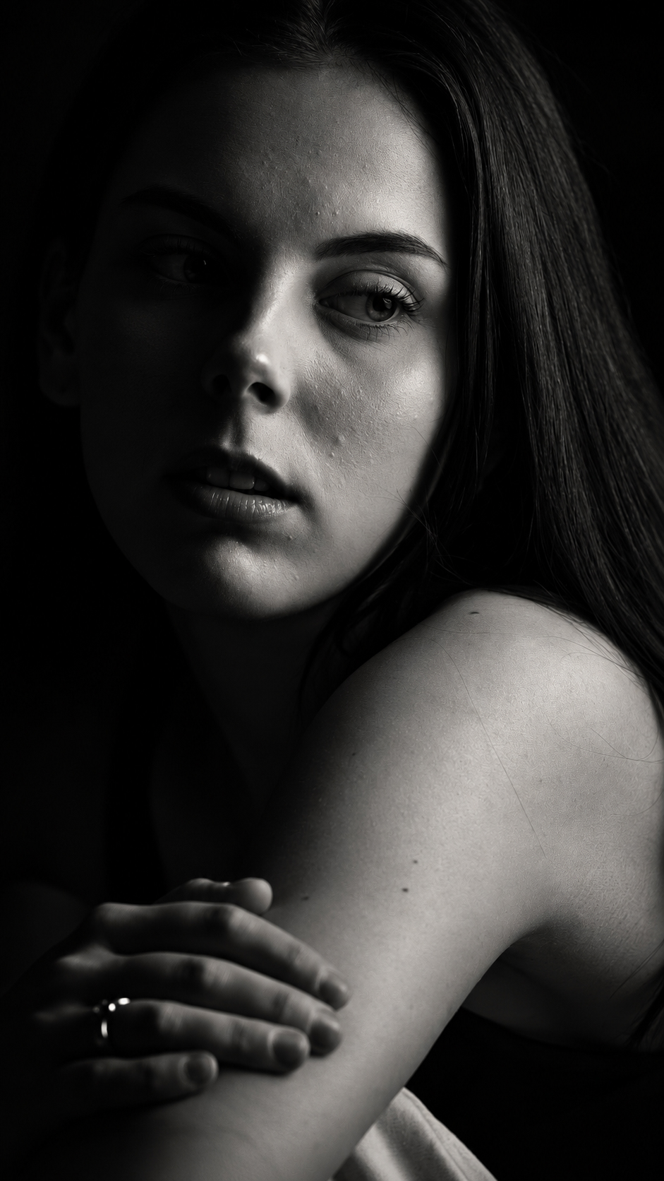A high-contrast black and white portrait of a woman looking away, lit from one side