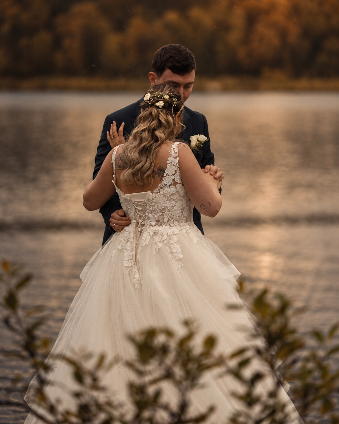 A bride and groom dancing outdoors by a lake in golden autumn light, holding hands