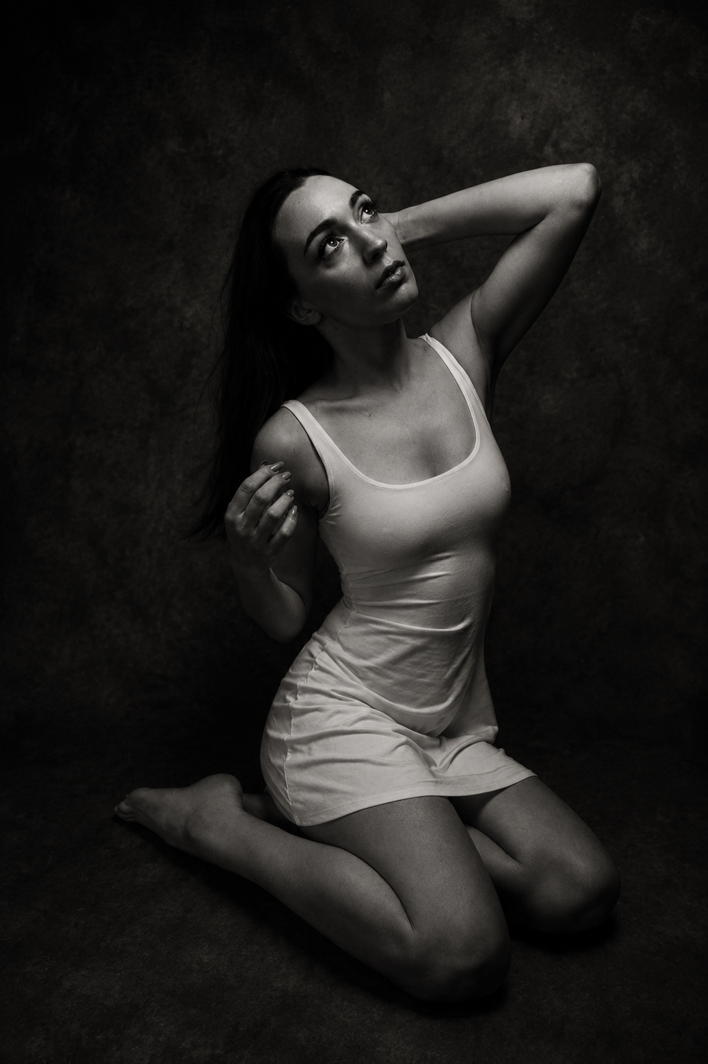 Black and white portrait of a woman kneeling against a dark backdrop