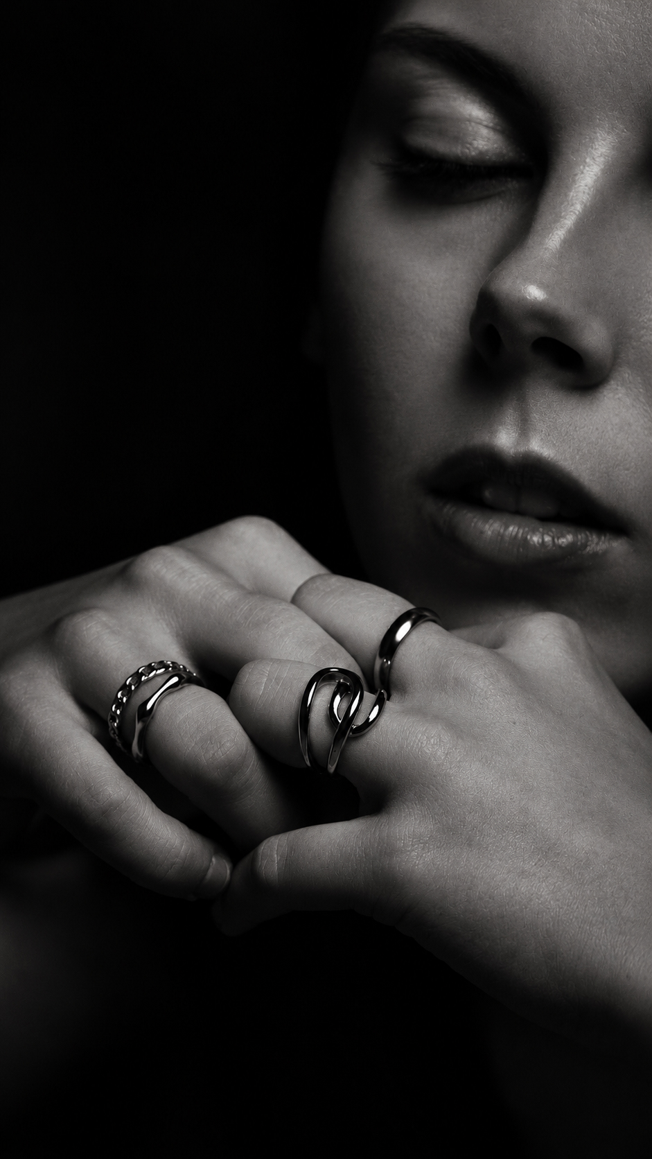 An extreme close-up of clasped hands near the chin, with rings, in dramatic studio lighting