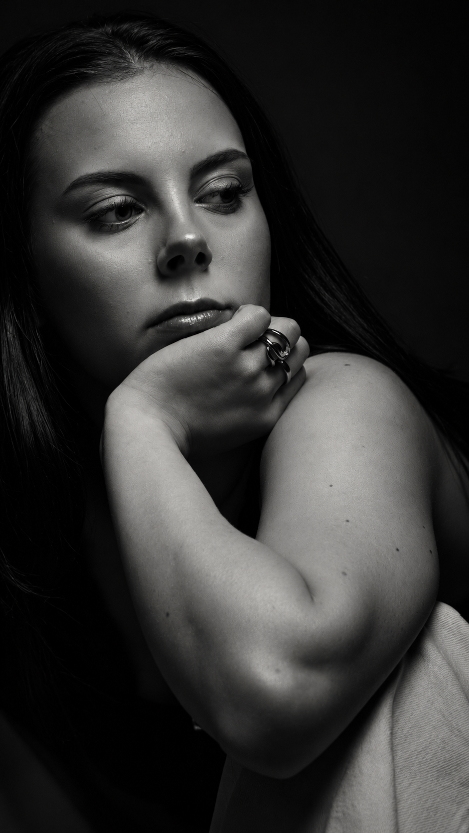 A young woman with dark hair resting her chin on her hand, studio portrait in dramatic light