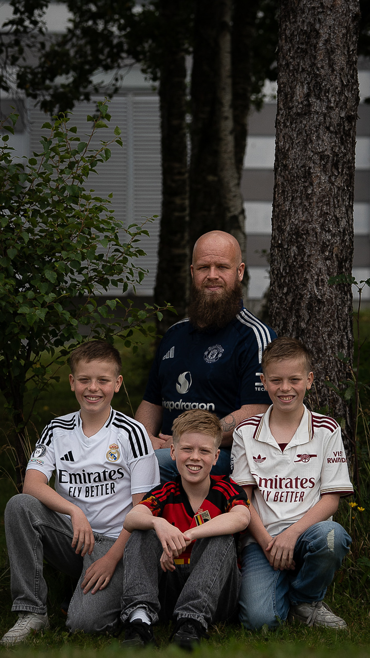 A bearded man and three boys in soccer jerseys sitting together outdoors
