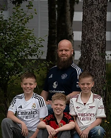 A bearded man and three boys in soccer jerseys sitting together outdoors