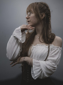 Linn-Kristin E. in profile wearing a white off-the-shoulder blouse, lit by soft grey daylight