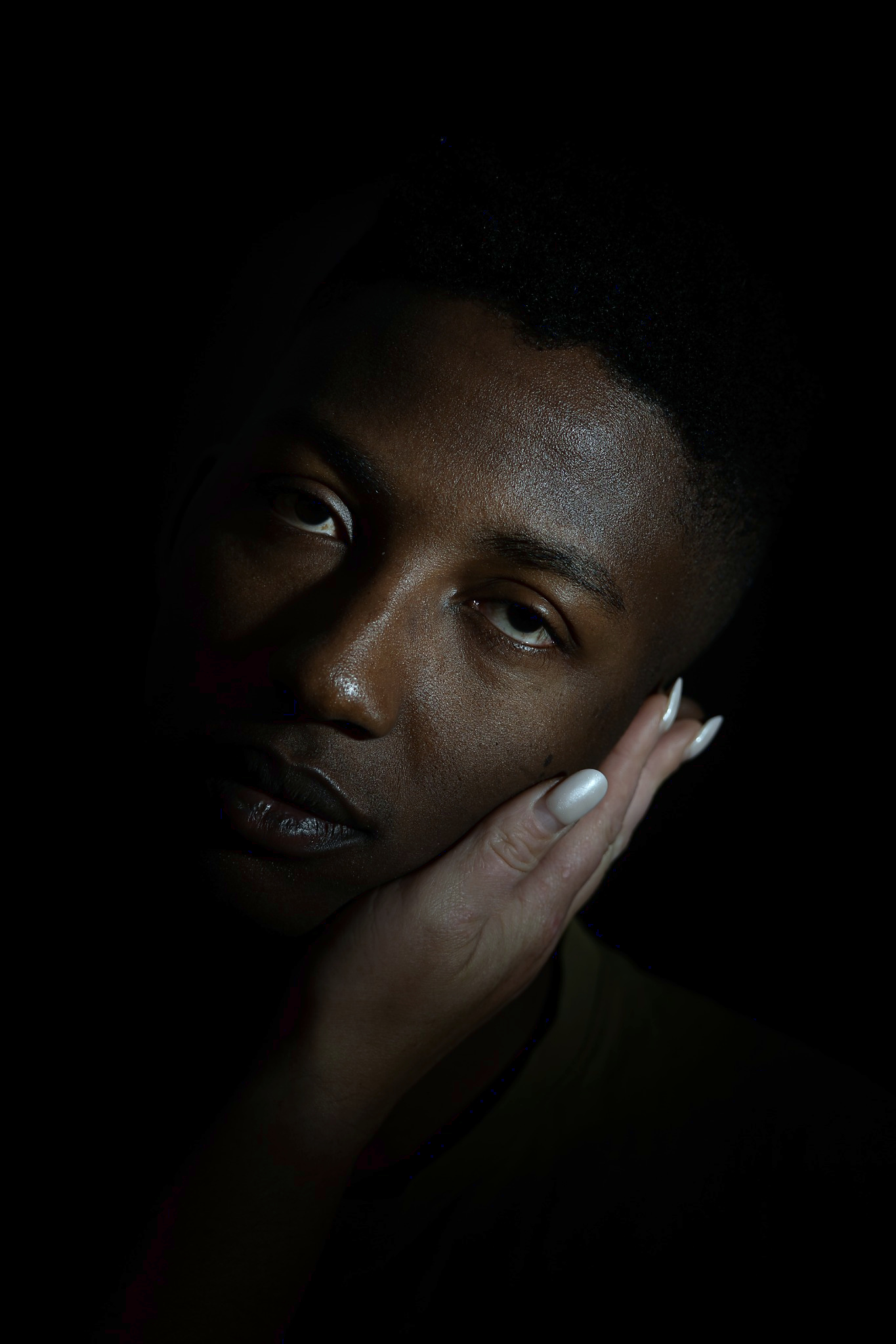 Dramatic low-key portrait of a person with a hand resting against the cheek, lit from the side