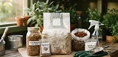 Close up of a wooden tabletop covered in bags of hardwood sawdust pellets, a spray bottle, and a container of mushroom grain spawn.