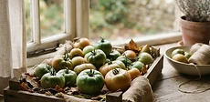 A wooden crate filled with various green and partially ripening tomatoes sitting on a rustic kitchen counter.