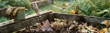 A close up view of a garden compost bin with layers of dry brown leaves and fresh green vegetable scraps mixed together.