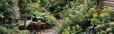 A small urban courtyard garden featuring vertical wooden planters on a brick wall, a bistro set on a light gravel path, and layered green foliage.