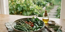 A close-up of freshly picked garden vegetables including leafy greens and snap peas sitting in a wooden bowl on a kitchen counter.