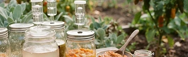 Several mason jars filled with chopped red and yellow peppers submerged in brine, sitting on a wooden kitchen counter next to a sea salt container.