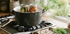 Close-up of glass mason jars filled with bright red tomatoes and sliced peaches sitting on a rustic wooden table next to a boiling water-bath canner.