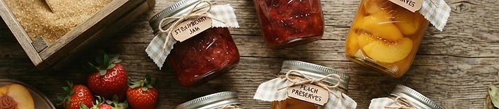 Mason jars of strawberry jam and sliced peaches on a rustic wooden table, sealed with metal lids and ready for the pantry.