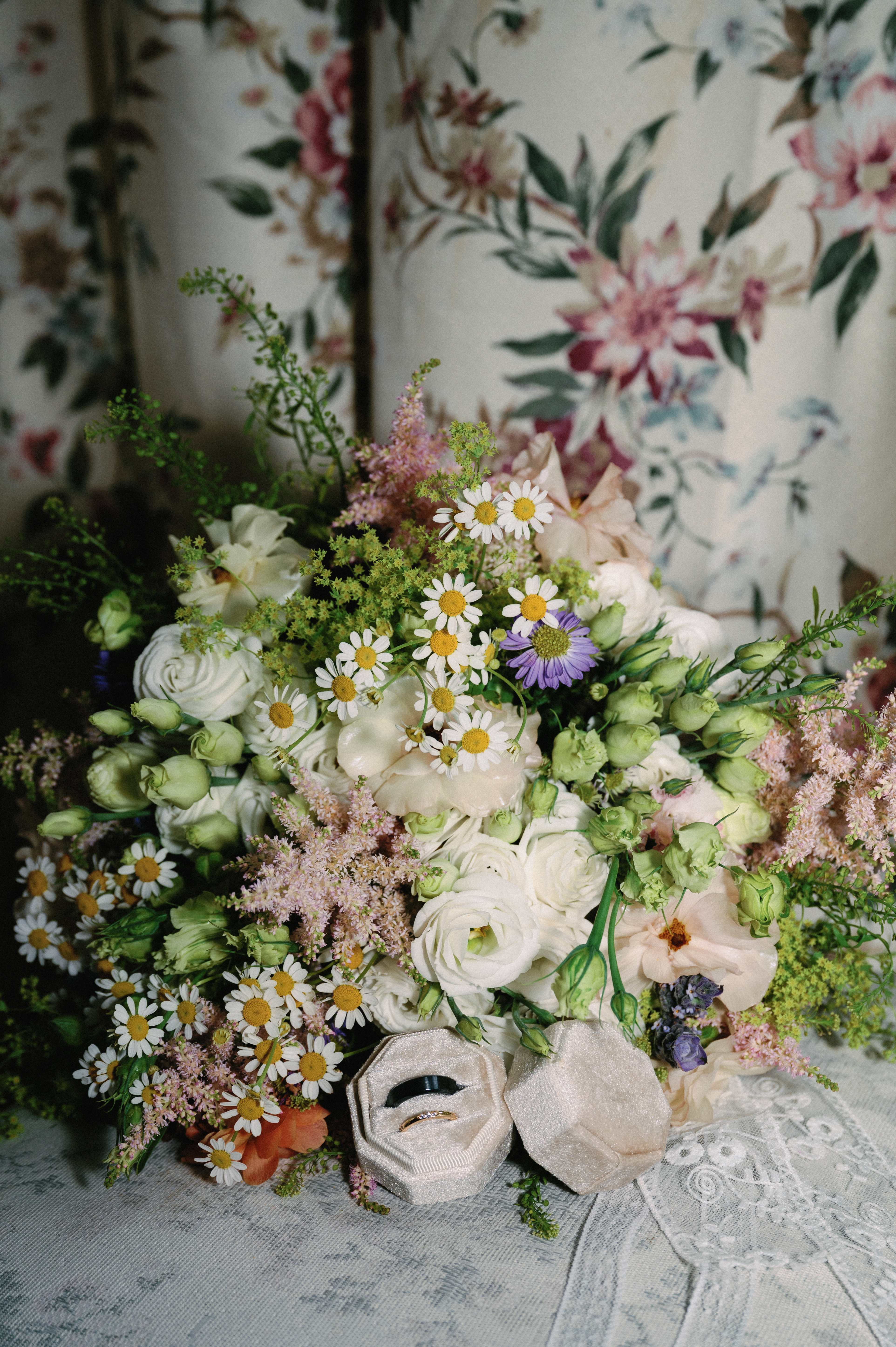 A lush bridal bouquet of wildflowers beside a velvet ring box holding two wedding bands