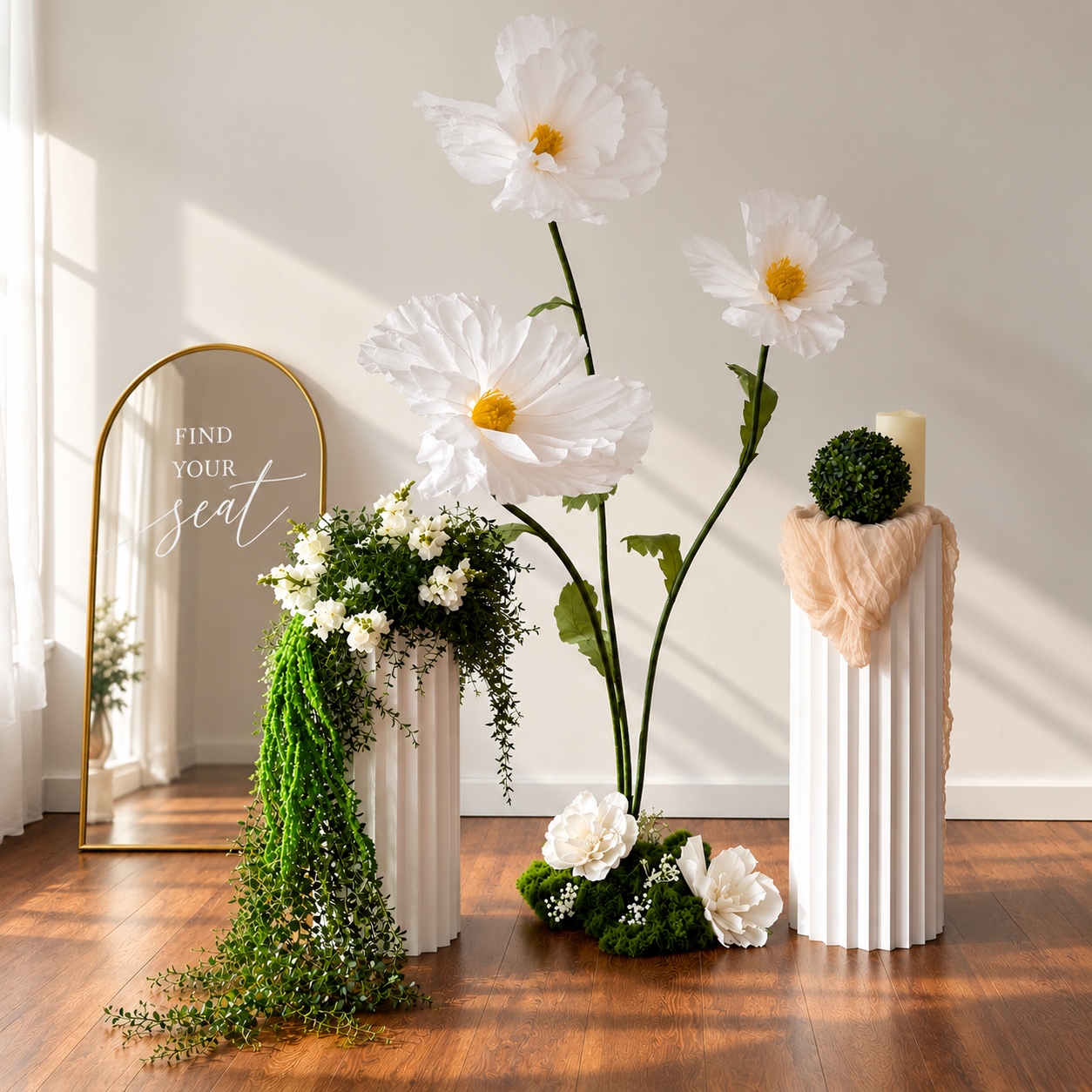 Statement piece vignette with white floral pillars, oversized paper flowers and a gold find-your-seat mirror