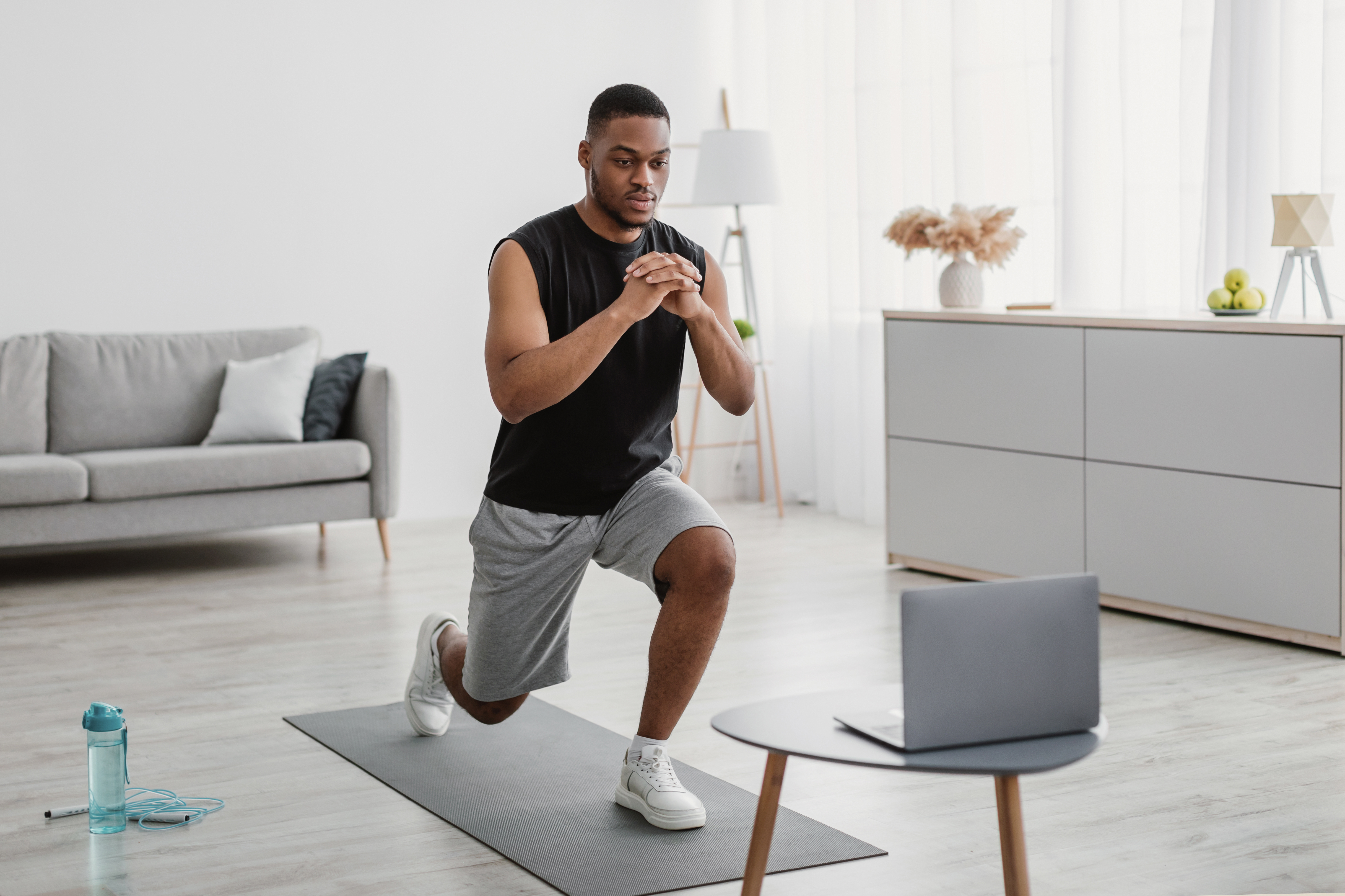 Man performing a lunge at home beside his laptop