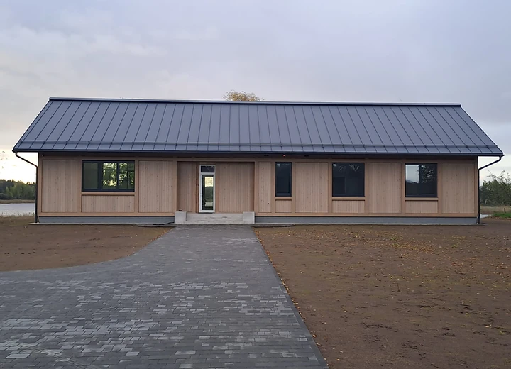 Mūsdienīga vienstāva koka māja ar stāvo metāla jumtu un tumšiem logu rāmjiem