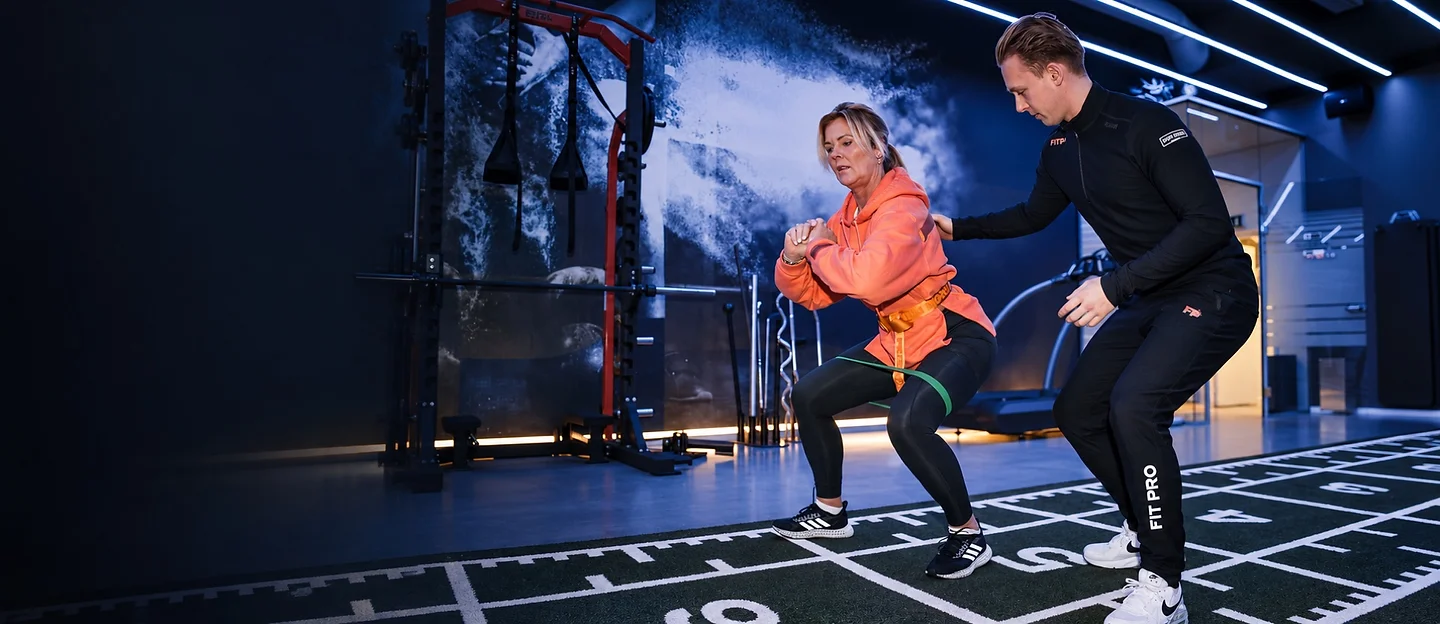 Trainer begeleidt een squat met weerstandsband tijdens Small Group HIIT bij FITPRO in Laren