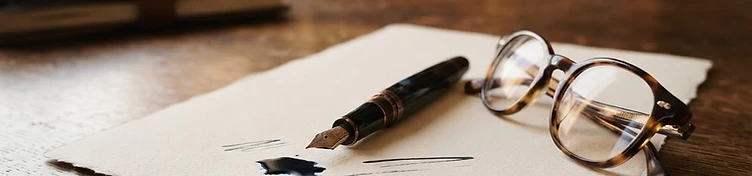Fountain pen, spectacles, and heavy paper on a wooden desk