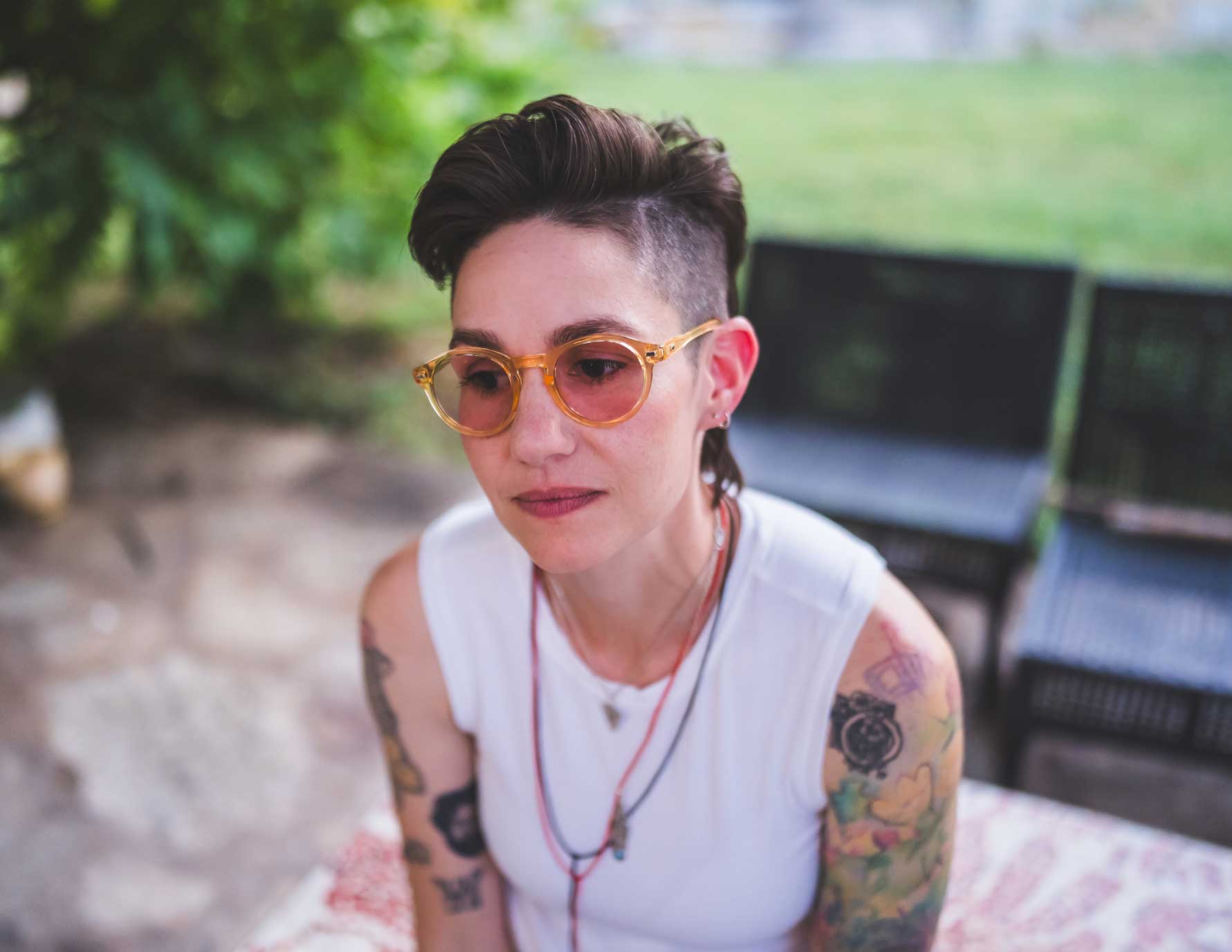 Emily McLoud laughing outdoors under tree, amber glasses, white muscle tank