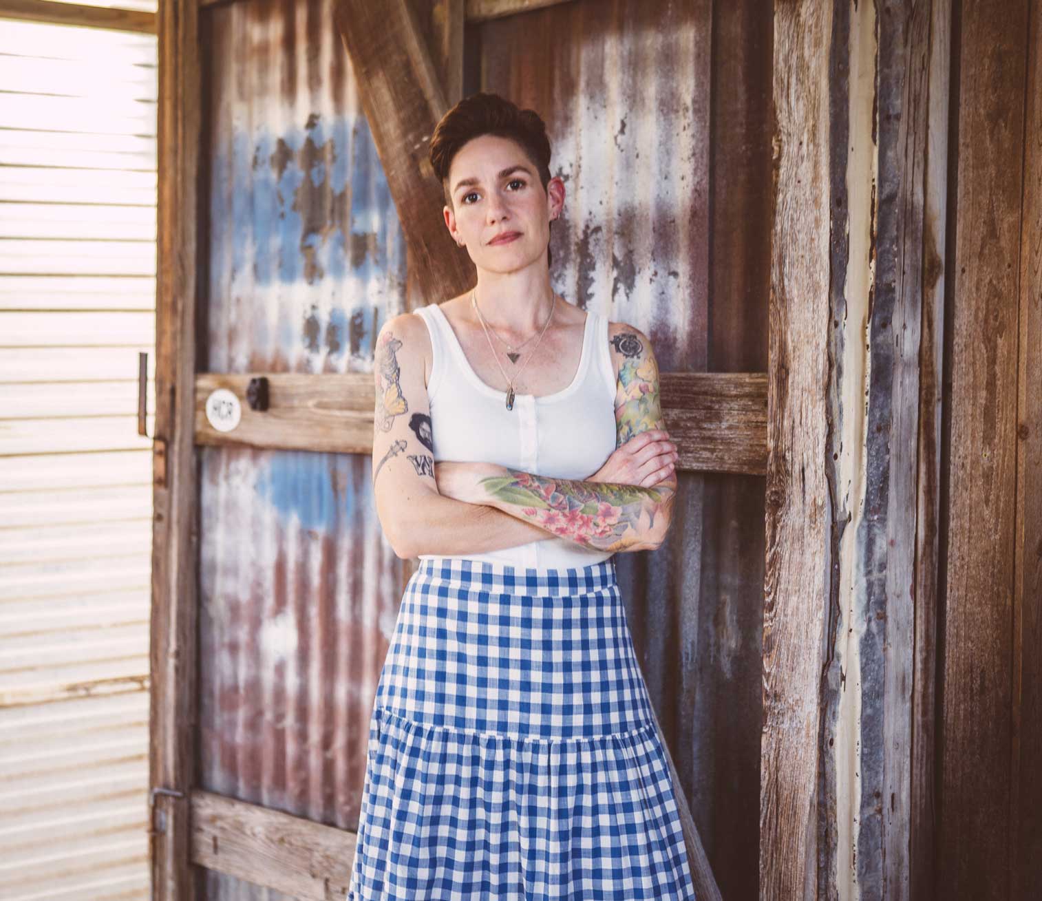 Emily McLoud arms crossed full-length portrait, weathered wood and metal backdrop