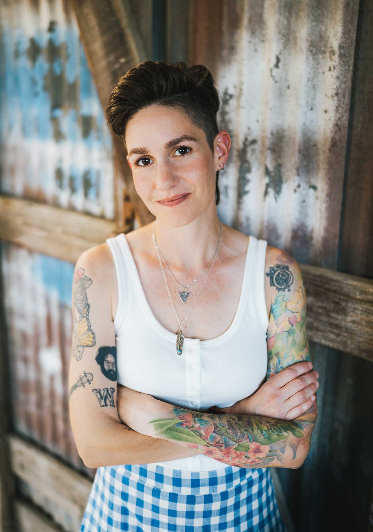 Emily McLoud smiling close-up portrait with arms crossed, rustic corrugated metal background