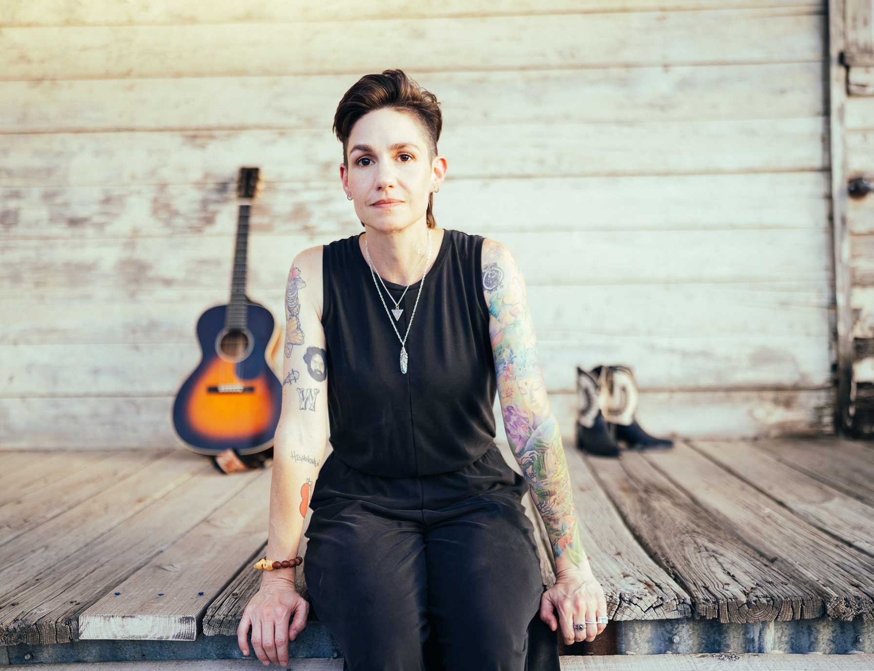 Emily McLoud sitting on porch ledge with guitar, looking off into distance