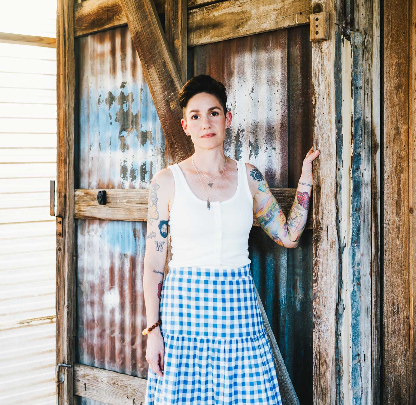 Emily McLoud leaning on weathered wooden door outdoors, country folk songwriter