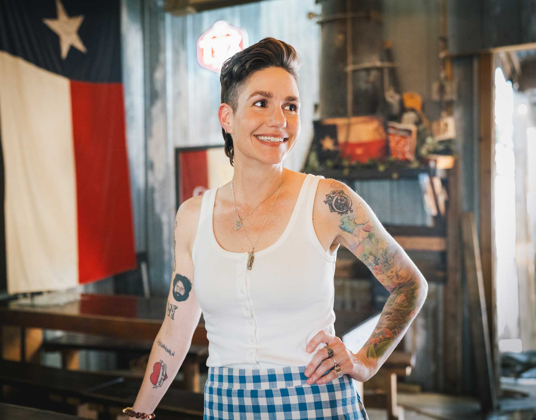 Emily McLoud press photo standing in gingham skirt at weathered barn door, Americana artist
