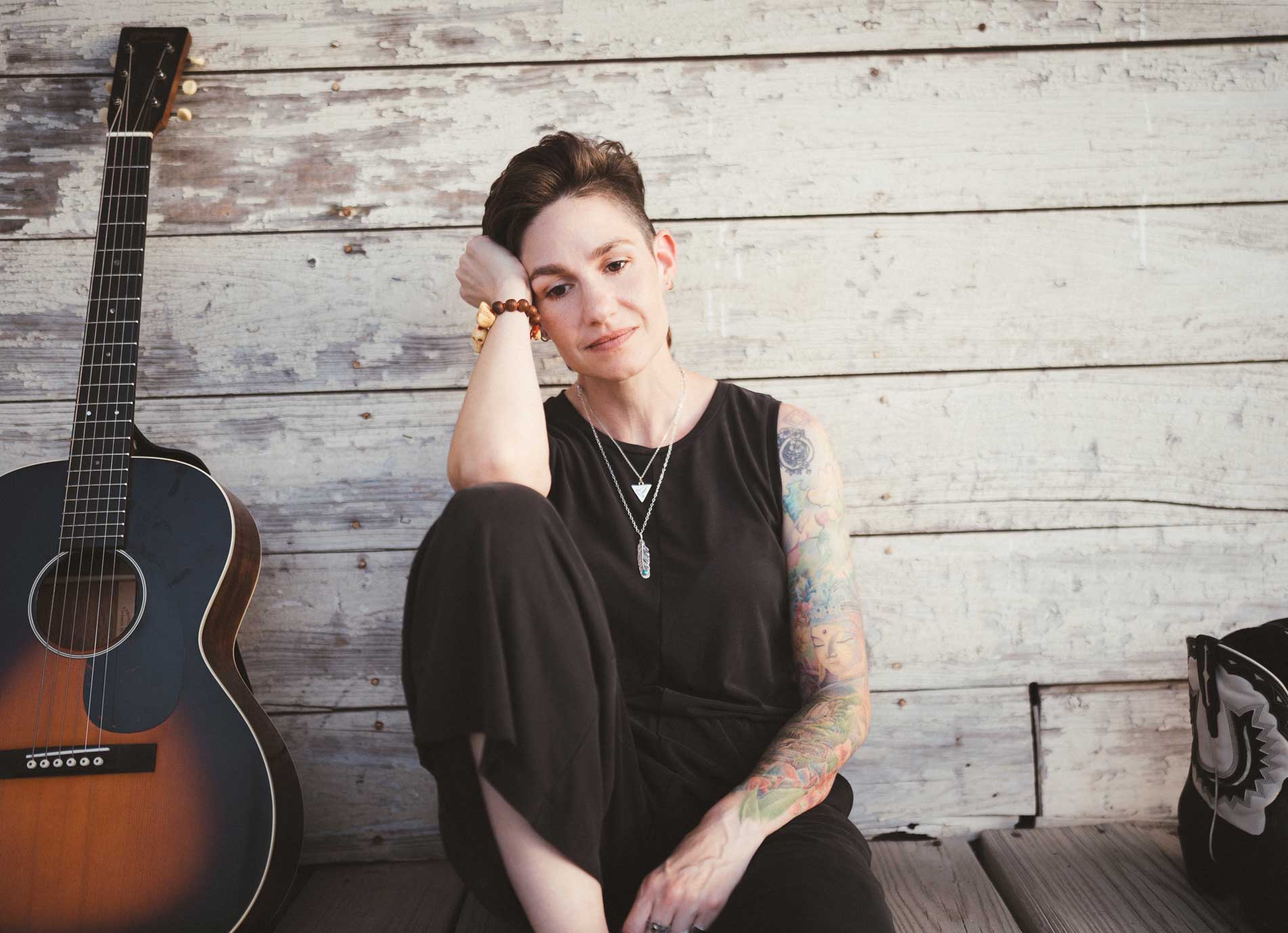 Emily McLoud seated on porch steps, guitar at side, boots visible, Americana songwriter