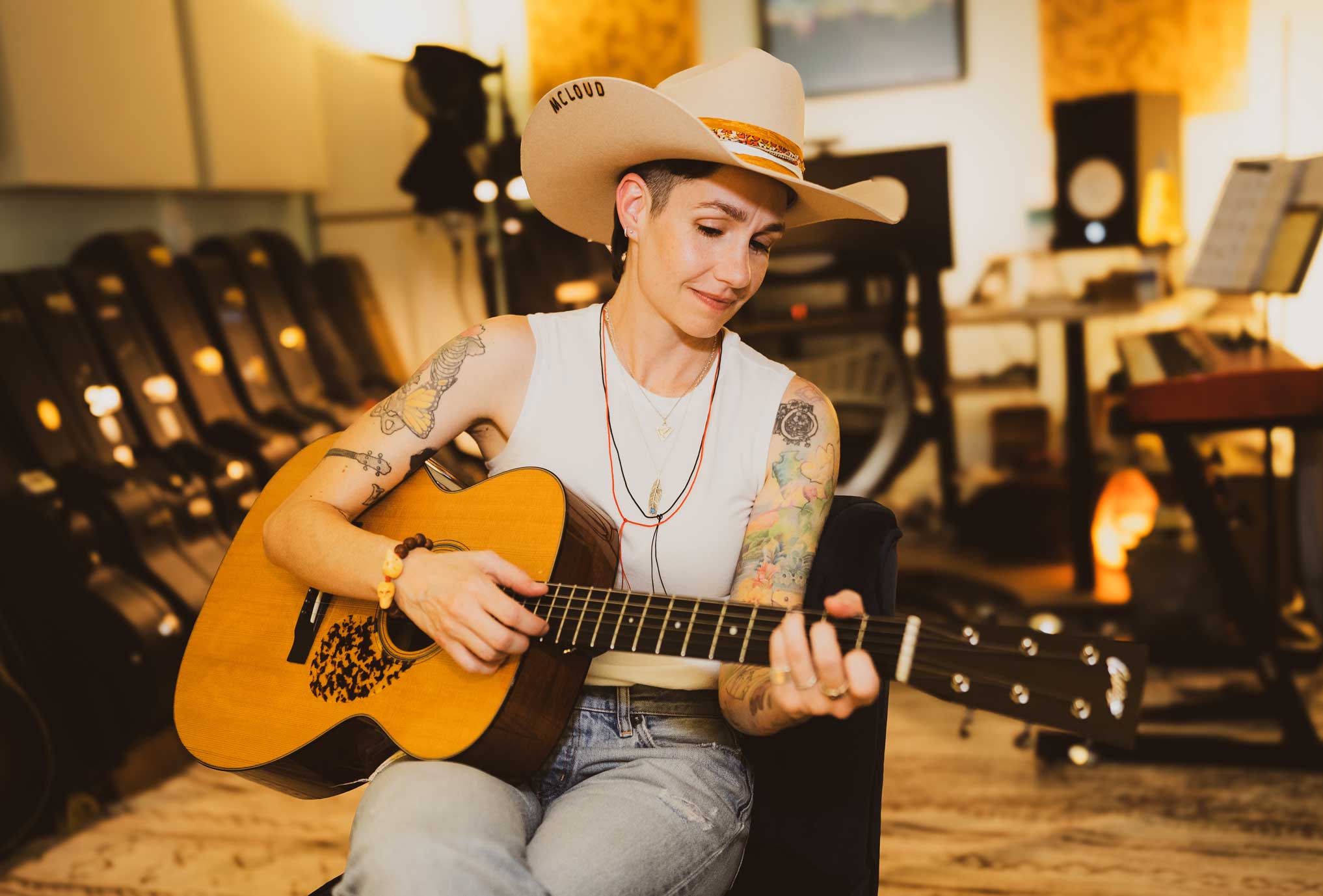 Emily McLoud playing guitar in recording studio with cowboy hat, warm golden light