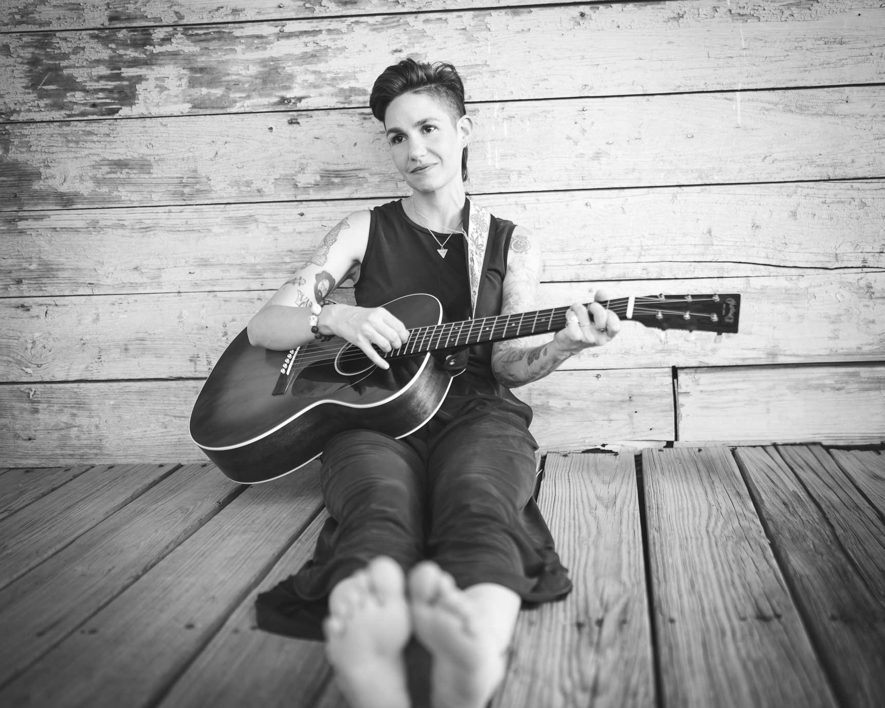 Emily McLoud black and white, seated playing guitar on wooden deck, relaxed