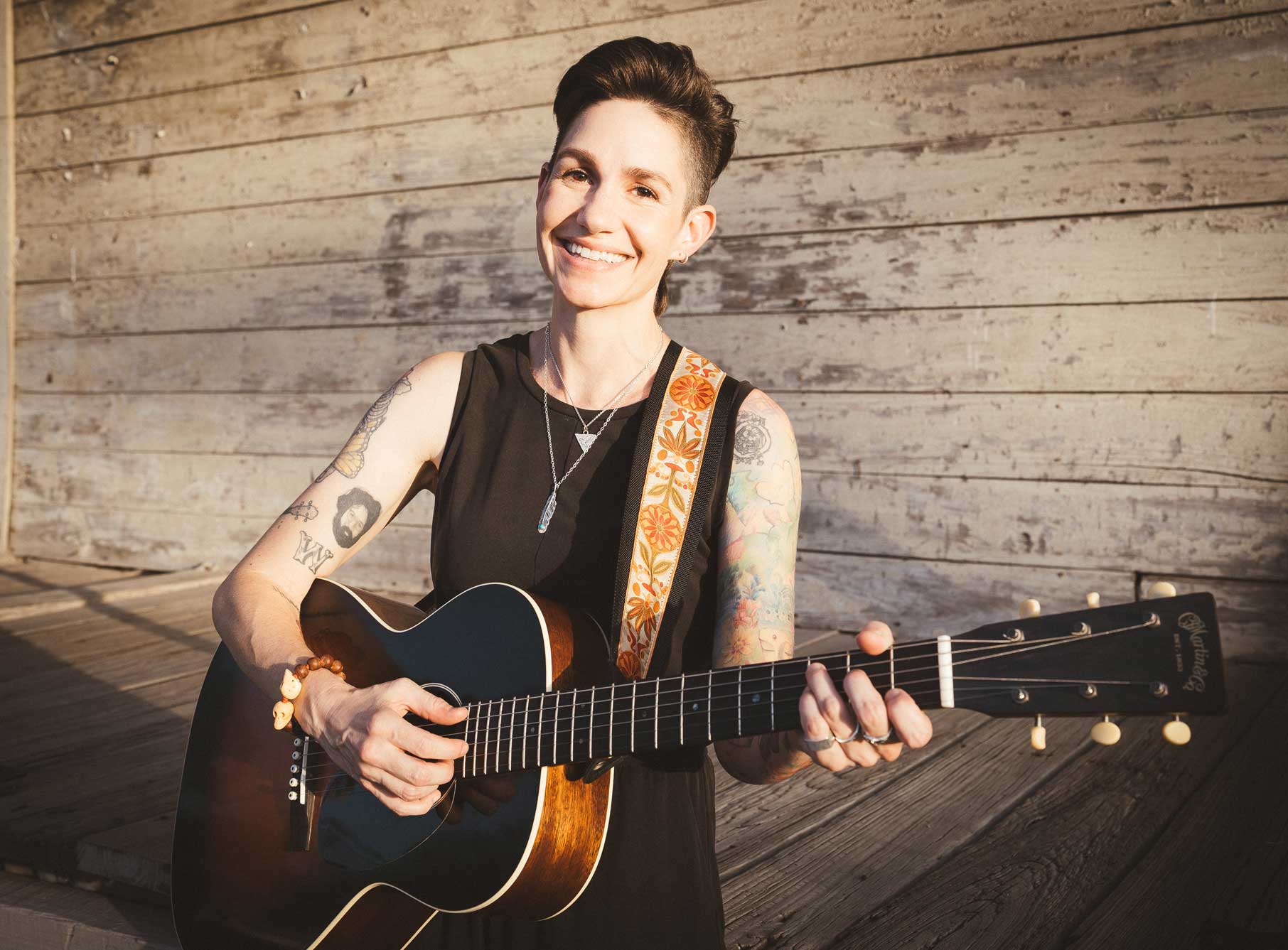 Emily McLoud playing acoustic Martin guitar and smiling on wooden porch, golden hour