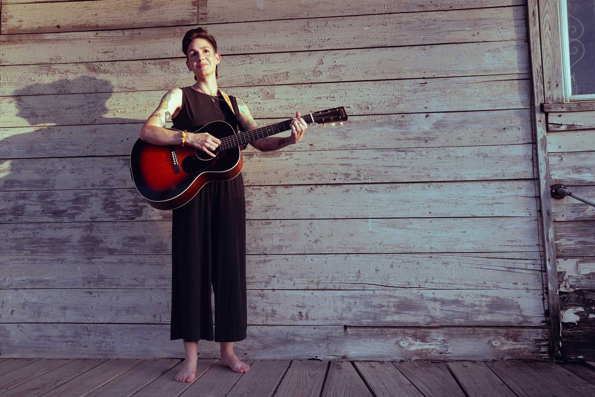 Emily McLoud playing guitar standing on weathered porch, color, country Americana