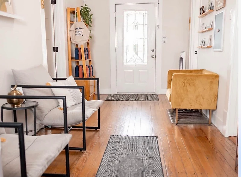 Interior view of the New Braunfels therapy office entryway, with grey and mustard-yellow seating and natural wood accents near the door.