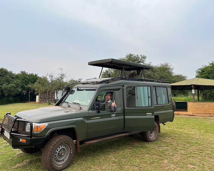 An Inland Africa safari guide giving a thumbs up from a custom 4x4 safari vehicle in Rwanda