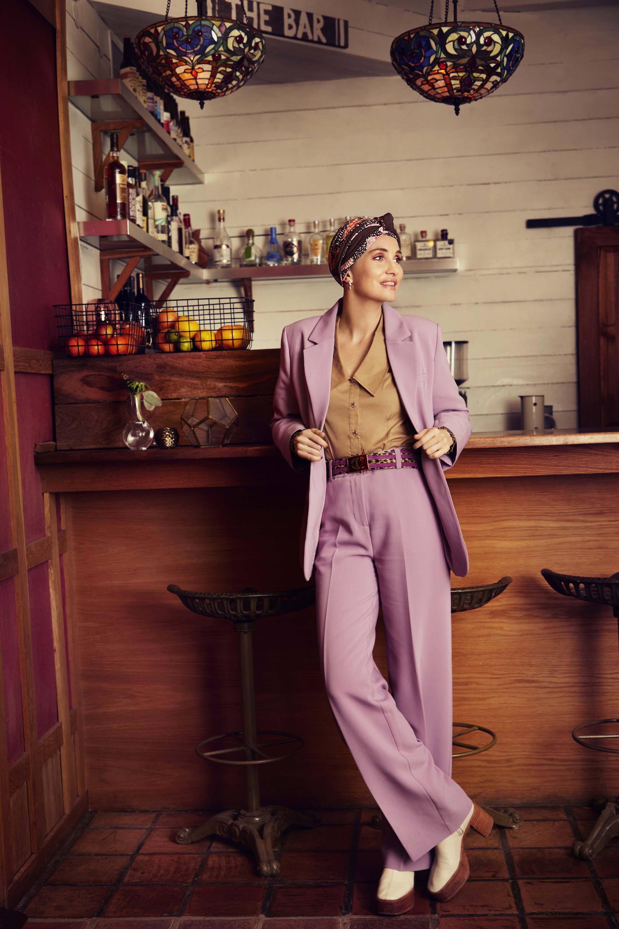 Woman in a lilac suit and patterned turban standing at a bar