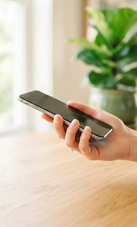 A hand holding a refurbished smartphone in bright natural light