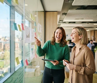 Two people reviewing marketing plans on a glass wall in a sunlit office