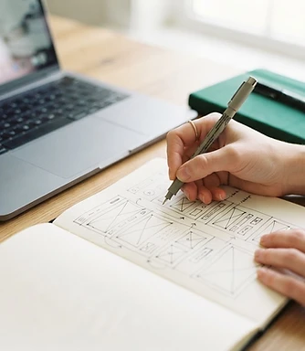 Close-up of hands sketching website wireframes beside a laptop