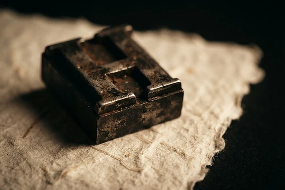 A heavy cast-metal type-block resting on fiber-rich ivory paper