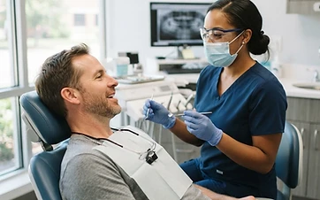 An American man in his mid-40s in a dental chair talking with a dental hygienist before treatment in a bright modern US dental office